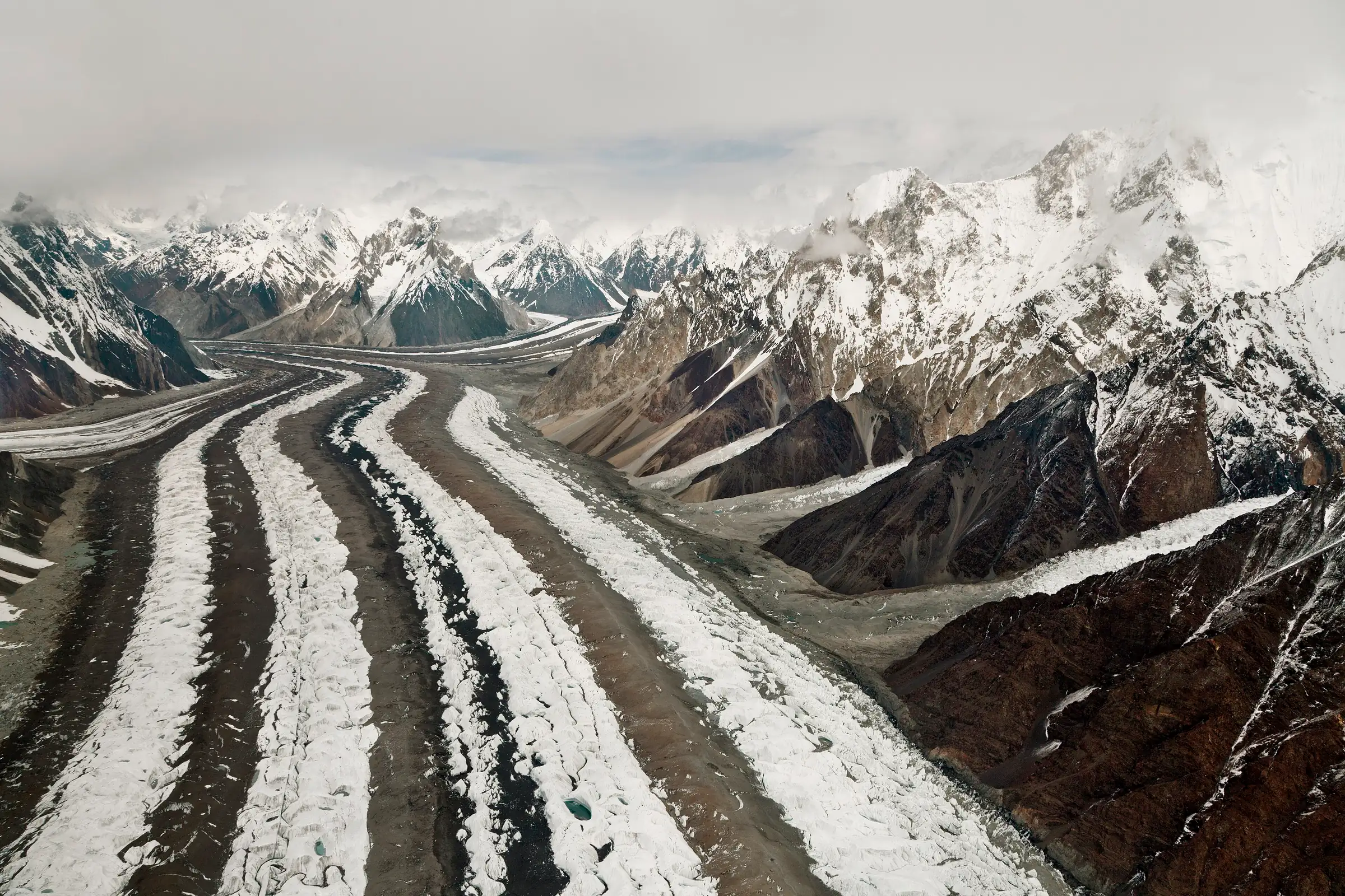 The striped ice of the Baltoro Glacier winding between snow peaks